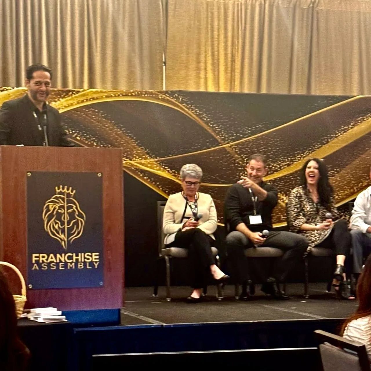 Rob Lancit seated on a Franchise Assembly panel, microphone in hand, pointing toward the audience