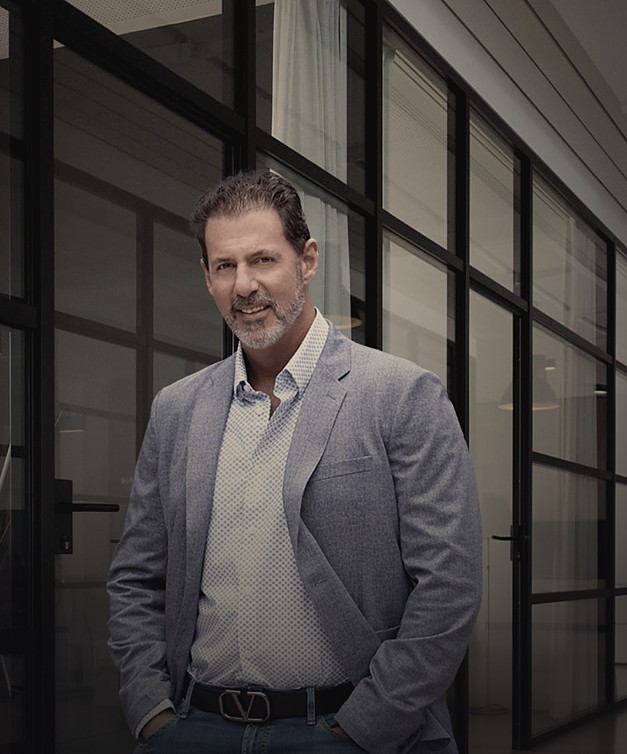 Rob Lancit in a gray blazer, hands in his pockets, in a glass-walled office hallway